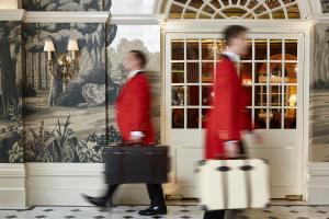 two men in red jackets walking in a room with luggage at The Goring in London
