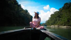 een vrouw die op het uiteinde van een boot op een rivier zit bij Hinkiori Inn - Hotel Manu in Pillcopata