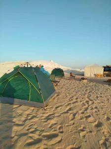 una tienda de campaña y sillas en una playa de arena en Tours of the White Desert, en Az Zabū