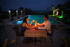 a man and woman sitting at a table with drinks at Le Kroma Villa in Phumĭ Prêk