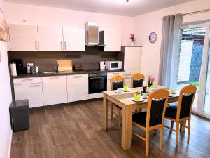 NEU "Poseidon" Papenburg ebenerdig rollstuhlgerecht 84 qm Neubau EBK Free Wifi NEU في بابينبورغ: مطبخ مع طاولة وكراسي ومطبخ مع دواليب بيضاء