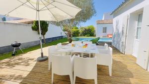 a table with white chairs and an umbrella on a deck at Superbe villa avec piscine dans le village de St Clément in Saint-Clément-des-Baleines