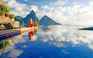 a woman sitting on the edge of a pool overlooking the water at Jade Mountain in Soufrière