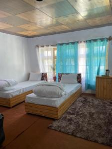 two beds in a room with blue curtains at Baltipa Homestay in Pānāmik