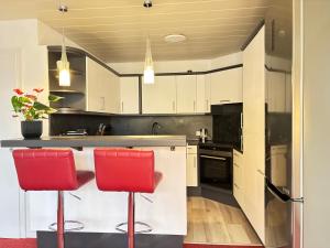 Serenity Stay Baiersbronn Kamin und Schwarzwaldblick في بايرسبرون: مطبخ مع خزائن بيضاء وكراسي الحانة الحمراء