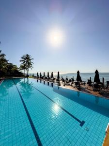 a swimming pool next to the ocean with people sitting at Casa no Condomínio Aguas d'Ajuda in Porto Seguro