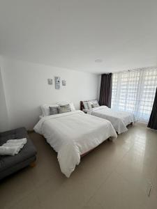 two beds in a white room with a couch at Apartamento Limón Azul in Sogamoso