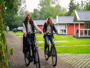 two women riding bikes down a brick path at Villa in Brabant with Spa and Sauna in Oirschot