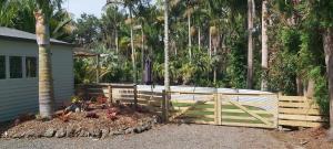 a wooden fence in front of a house with palm trees at Darwin Cottage in Kerikeri