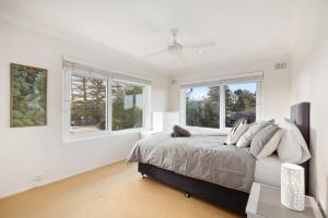 Un dormitorio blanco con una cama y ventanas. en Royal Surf - Beach Front Paradise, en Narrabeen