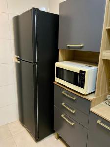 a black refrigerator in a kitchen with a microwave at Seu Lar de Praia p Família e amigos 400m do Mar em Condomínio in Praia Grande