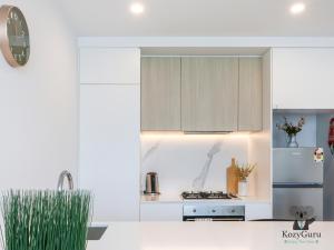 a white kitchen with a stove and a refrigerator at KozyGuru | Box Hill | Elegant City Hideaway in Box Hill