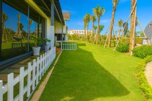 a white fence next to a house with palm trees at Happy Garden Hồ Tràm in Ho Tram