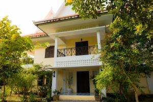a white house with a balcony and trees at La maison bleue BTB in Phumĭ Kâmpóng Âmpĭl