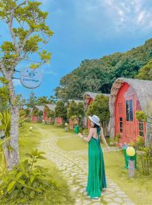 Una mujer con un vestido verde y una casa roja. en Cô Tô Village, en Ðiền Xá