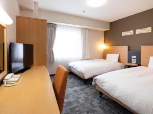 a hotel room with two beds and a desk with a television at Comfort Hotel Hachinohe in Hachinohe
