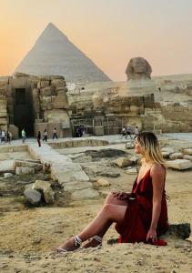 Una mujer con un vestido rojo sentada frente a las pirámides. en Noya Pyramids view hotel, en El Cairo