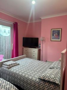 a bedroom with pink walls and a bed and a television at Paignton seafront Apartment with Private Garden ,FREE Private Car Space FREE WIFI ,No kitchen but Fridge Tea coffee Towels YES Double & Single bed YES Reception to help you YES Opposite the Beach Yes in Paignton +22 photos