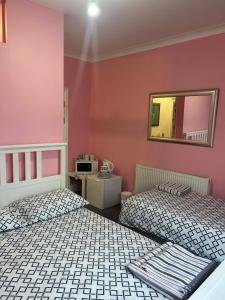 two beds in a room with pink walls and a mirror at Paignton seafront Apartment with Private Garden ,FREE Private Car Space FREE WIFI ,No kitchen but Fridge Tea coffee Towels YES Double & Single bed YES Reception to help you YES Opposite the Beach Yes in Paignton