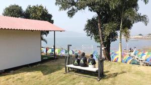Pawna Tent Camp by Maitri Pawna Lake في Kolvan: يجلس شخصان على مقعد تحت شجرة