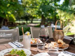 a wooden table with plates of food and a glass of wine at Hotel Novotel Domaine de Maffliers - Paris Val-d'Oise in Maffliers