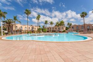 a large swimming pool with palm trees and houses at Oasis Penthouse Maspalomas in Maspalomas
