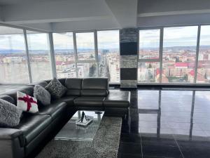 a living room with a leather couch and large windows at Sky17 Penthouse Sibiu in Şelimbăr