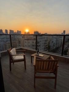 a balcony with two chairs and a table and a sunset at Sunset Home - Netanya Roof & Sea View in Netanya