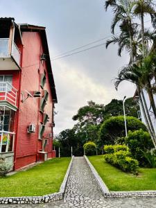 a red building and a palm tree next to a street at Enseada Azul Home in Guarapari