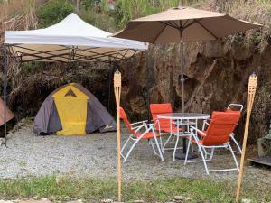 una mesa y sillas bajo una sombrilla junto a una tienda de campaña en Camping Dos Buhos, en Líbano