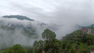 a misty mountain with trees and buildings in the background at Amazing Valley View in Kasauli