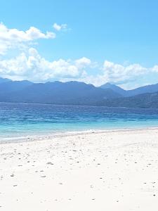 a beach with blue water and mountains in the background at Kampung Meno Bungalows in Gili Meno