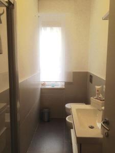 a bathroom with a toilet and a sink and a window at Lilly Rose Apartment in Alba