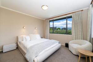 a white bedroom with a bed and a chair and a window at Beacon Point Lakeview Escape - Spacious - Stylish in Wanaka +17 photos