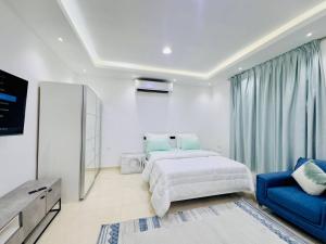 a white bedroom with a bed and a blue chair at Fully Furnished Studio Near Exibition Center Abu Dhabi in Abu Dhabi