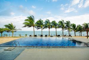 a swimming pool next to the beach with palm trees at Peacock Beach Resort- Hambantota in Hambantota