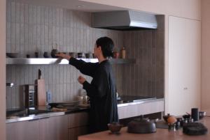a woman in a kitchen reaching for a pot on a shelf at 雲居月-kumoizuki- in Ginowan