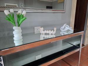 Un estante de cristal con un jarrón de flores y un espejo. en Sabs Place, en Gillitts