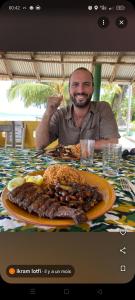 KachiouaneAnkel campement的一位男士坐在桌边，面前摆着一盘食物