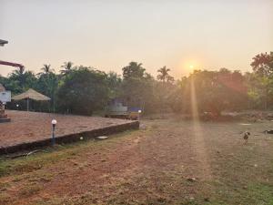 Ein unbefestigtes Feld mit der untergehenden Sonne im Hintergrund in der Unterkunft Farm House Shetgeri in Ankola