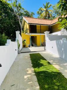 a yellow house with a white fence and a yard at Vintage 83 Tangalle in Tangalle