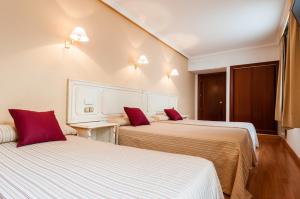 two beds in a hotel room with red pillows at Hotel Victoria in Linares