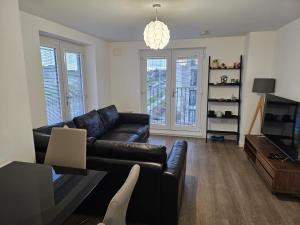 a living room with a black leather couch and a television at Stylish 2-Bed Flat with Open-Plan Living plus Parking in Edinburgh