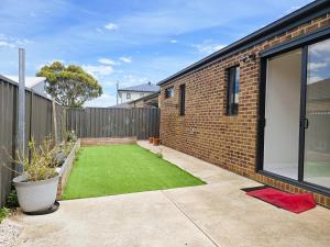 Modern 4BR Home Spacious & Family Friendly في Melton South: فناء خلفي صغير مع منزل من الطوب مع حديقة