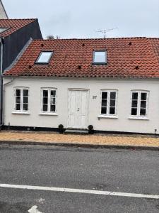 a white house with a red roof on a street at Charmerende byhus midt i Assens in Assens