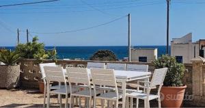 een witte tafel en stoelen met de oceaan op de achtergrond bij Villetta Mirion in Marina San Gregorio