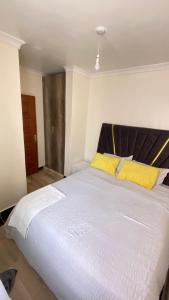 ThikaSunrise apartment next to bullys hotel的一间卧室，里面有一张白色的大床，配着黄色的枕头。