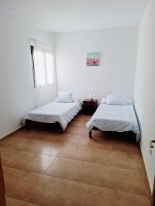 two beds in a room with white walls and wooden floors at La Caracola in La Santa