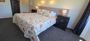 a bedroom with a bed with a floral bedspread and a nightstand at Bumble Bee Cottage in Kerikeri +24 photos