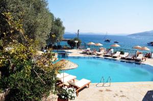 a swimming pool with chairs and umbrellas next to the ocean at Omar Hotel & Suites in Torba